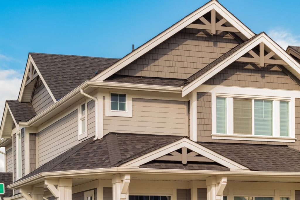 how long does a roof last close-up view of a modern two-story house with gray siding, white trim, and multiple gables under a clear blue sky. Large windows are visible on the upper floor.