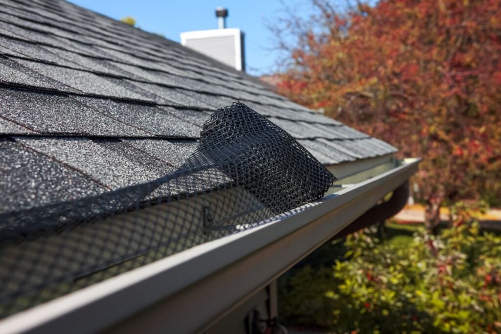 gutter screens A black mesh gutter guard is partially installed on a house’s roof gutter, with autumn trees and a blue sky visible in the background.