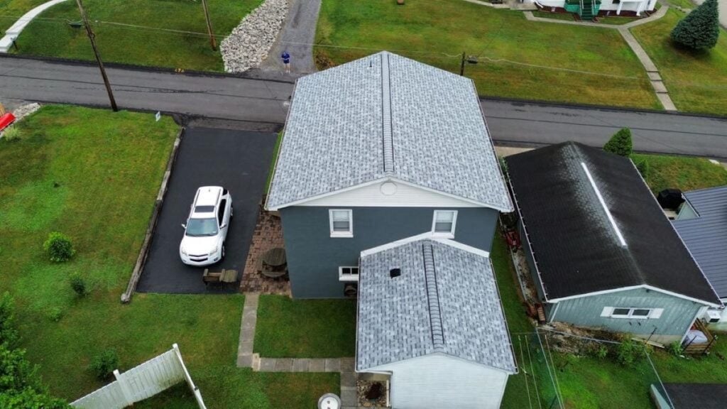 roof underlayment Aerial view of a gray two-story house with a matching gray extension, a white car parked on a black driveway, and surrounding green lawns in a residential neighborhood.