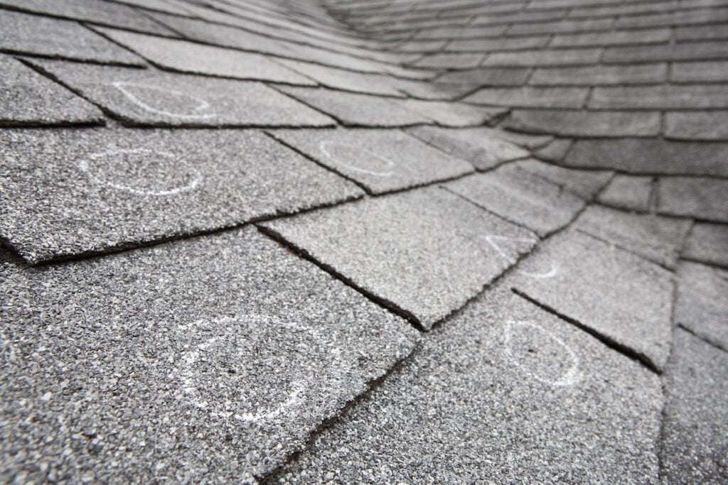 Close-up of gray asphalt roof shingles with several white chalk circles marking spots of damage or wear