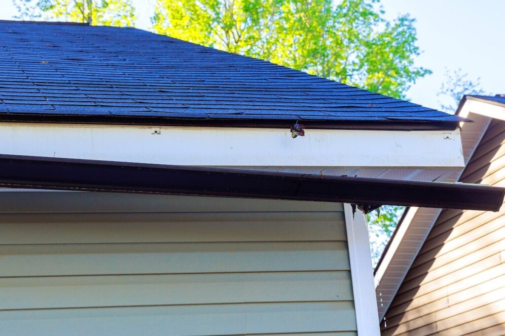Broken rain gutter on roof of house after hurricane damages