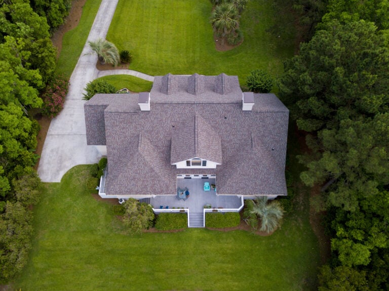 roof types Aerial view of a large house with a gray roof, surrounded by green grass, trees, and shrubs; a driveway curves to the left side of the property.