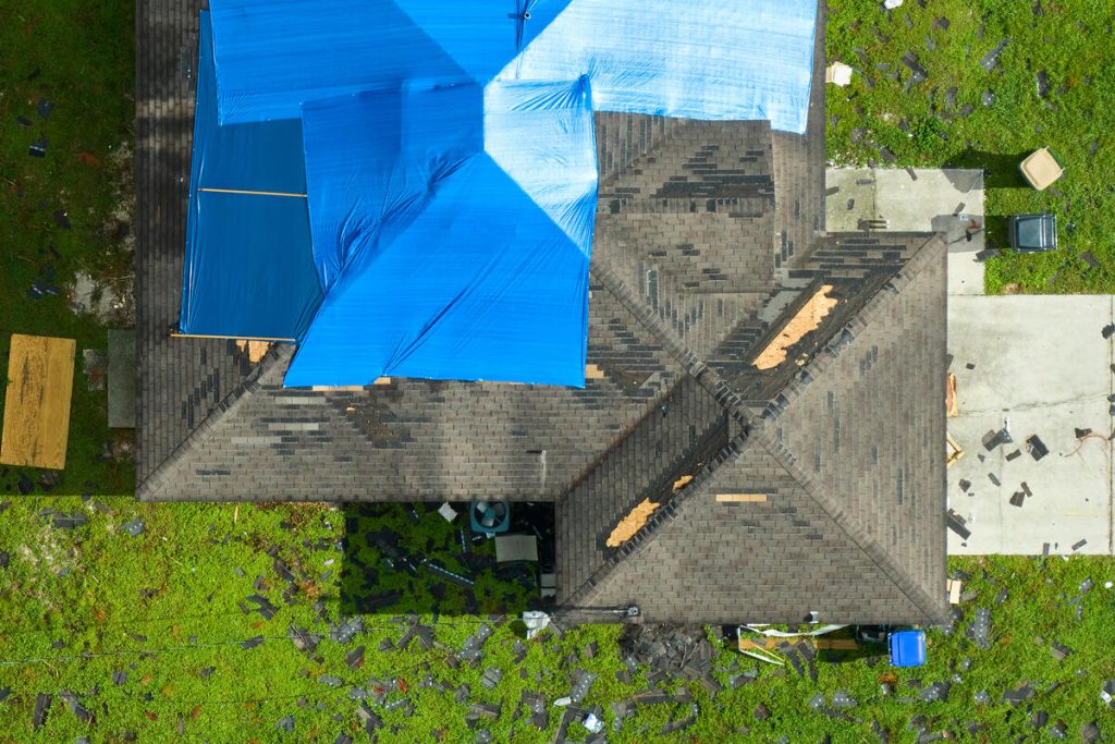 Aerial view of a residential roof with missing shingles and a large blue tarp covering a damaged section.